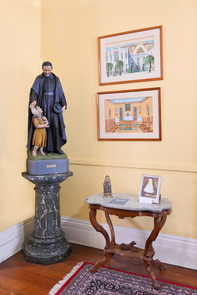 Statue on pedestal with two framed illustrations on the wall and small table